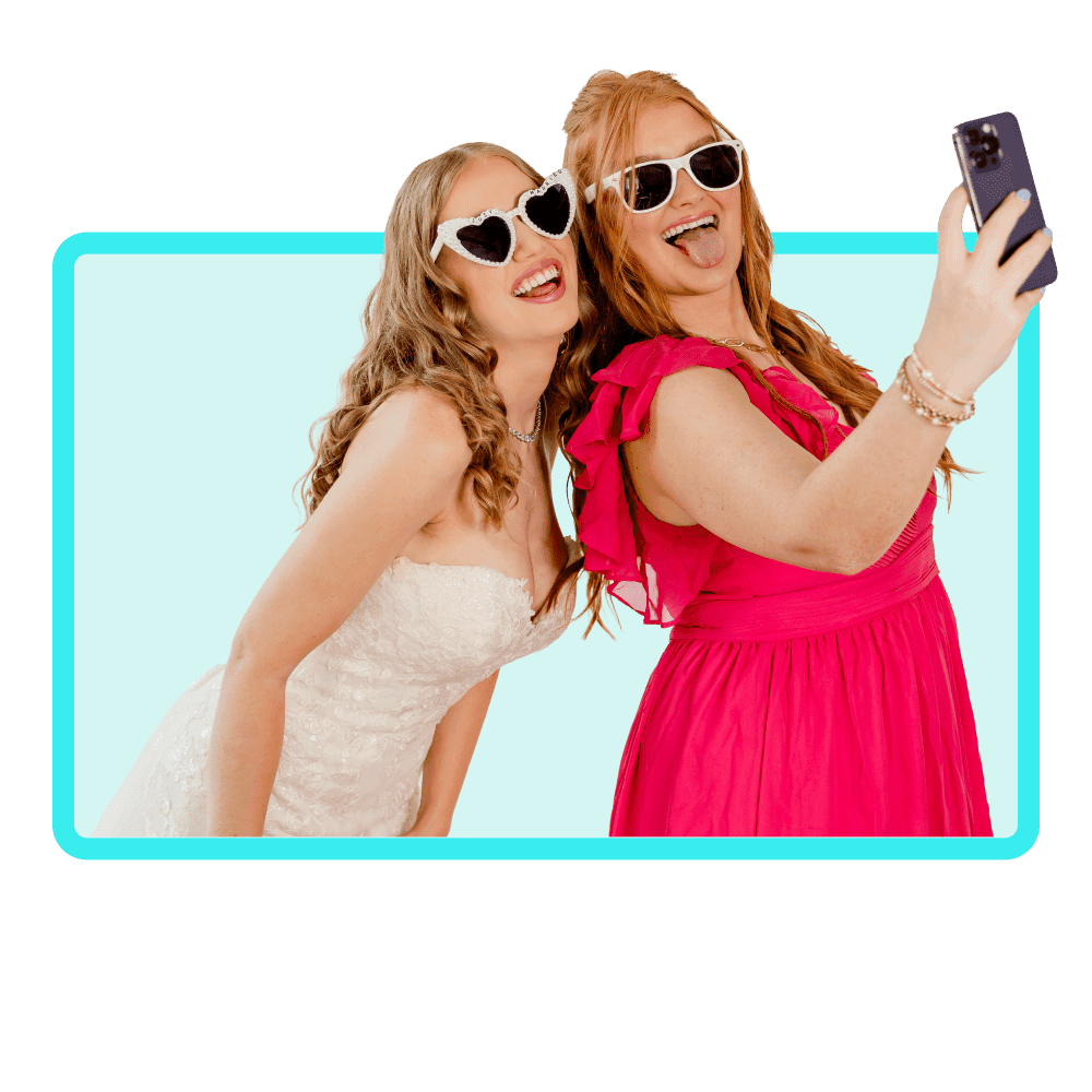 two women bride and guest in pink/red dresses taking a selfie with sunglasses.